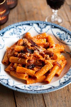 a blue and white plate topped with pasta covered in sauce next to a glass of wine