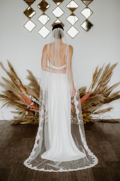 the back of a bride's wedding dress with a veil over her head and flowers on the floor