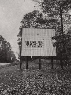 a large sign sitting on the side of a road in front of some tall trees