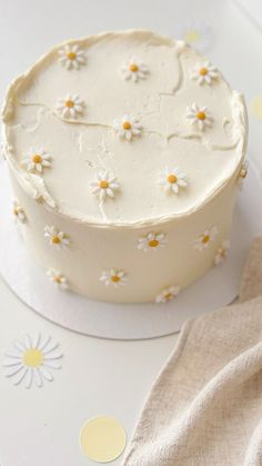 a cake with white frosting and daisies on it sitting on a plate next to a napkin