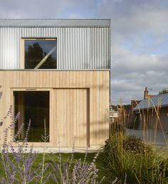 a house made out of wood and metal is surrounded by purple flowers in the foreground