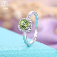 a ring with a heart shaped green stone surrounded by diamonds on top of a blue box