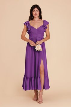 a woman wearing a purple dress with ruffles on the shoulders and side slit