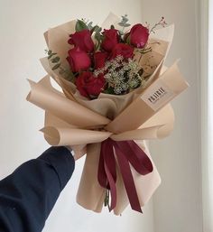 someone is holding a bouquet of red roses in their left hand and wrapped with brown paper