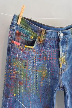 a pair of blue jeans with multicolored stitchs on them hanging from a clothes line