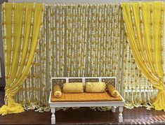 a white bench sitting in front of a yellow curtained wall with pillows on it