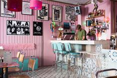 a woman sitting at a bar in a pink room with lots of pictures on the wall