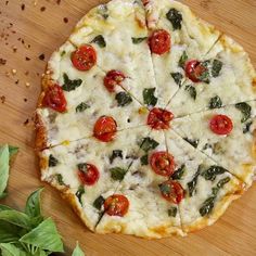 a pizza sitting on top of a wooden table covered in cheese and toppings with leaves