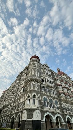 a large building with many windows and balconies on the top floor under a cloudy blue sky