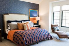 a bedroom with blue and orange bedding, two chairs and a painting on the wall