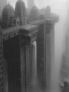 black and white photograph of skyscrapers in the foggy city with an arch between them