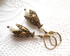 Victorian style dangle earrings in white and bronze, made of white teardrop glass faux pearl beads, oxidized brass and bronze beadcaps and beads. The lever back earwire is made of oxidized brass. The length of the earrings without the earwire is ± 2.5 cm. (1 inch) For other jewelry please visit our shop: http://www.minouc.etsy.com We also combine shipping with our other Etsy shop where we sell vintage fabrics and finds from Germany and France: http://www.minoucbrocante.etsy.com Romantic Earrings, White Pearl Earring, Vintage Style Earrings, Teardrop Dangle Earrings, Filigree Earrings, Unusual Jewelry, Red Earrings, Pearl Earrings Dangle, Opal Earrings