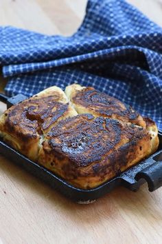 some food is sitting in a black pan on a wooden table next to a blue towel