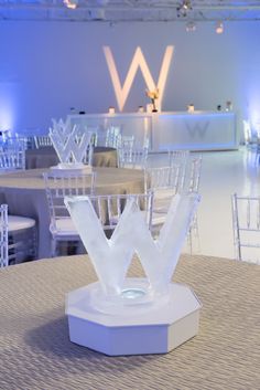 the table is set up for an event with white chairs and round tables in the background