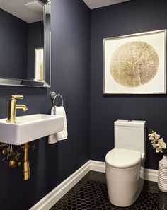 a white toilet sitting next to a sink in a bathroom under a framed art piece