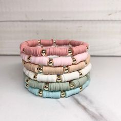 four different colored leather bracelets with gold clasps on white wood planked background