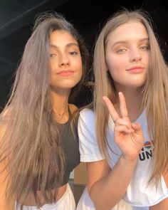 two young women making the peace sign with their fingers while standing next to each other