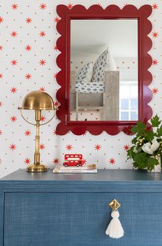 a blue dresser with a red mirror on it and a gold lamp next to it