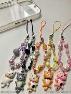 several key chains with different colored cats on them next to a cell phone and other items