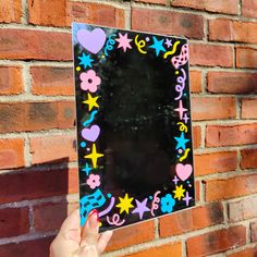 a person holding up a mirror in front of a brick wall with hearts and stars on it