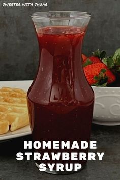 homemade strawberry syrup in a pitcher next to strawberries and waffles on a plate