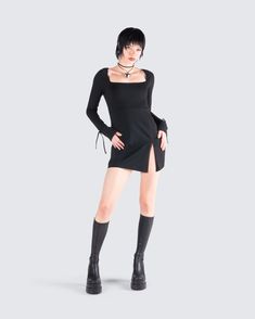 a woman in a black dress and boots posing for the camera with her hands on her hips