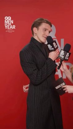 two people standing next to each other with microphones in front of red wall and one person holding an award