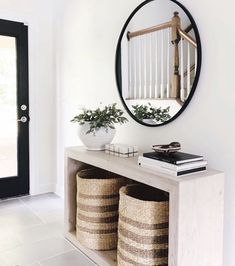 a white entryway with two baskets and a round mirror on the wall above it