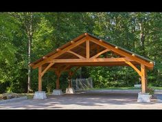 a wooden pavilion in the middle of a parking lot with trees around it and bushes on either side