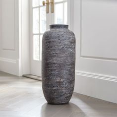 a large gray vase sitting on top of a hard wood floor next to a window