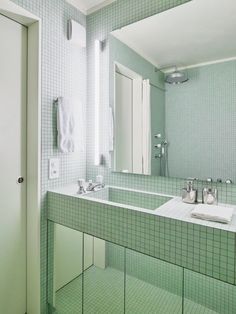 a green tiled bathroom with two sinks and mirrors