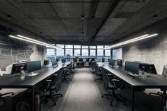 an office with multiple desks and computer screens on the wall, along with large windows