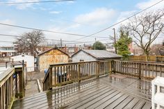 a wooden deck with chairs on it next to trees and buildings in the back ground