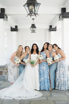 a group of women standing next to each other in front of a white building holding bouquets