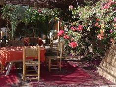 an outdoor dining area with pink flowers and greenery on the walls, table and chairs