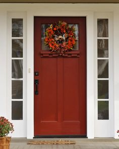 a red front door with two potted plants on the side and an autumn wreath