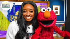 a woman with long black hair is holding a sesame character