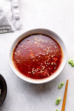 a white bowl filled with red sauce next to chopsticks and a bag of rice