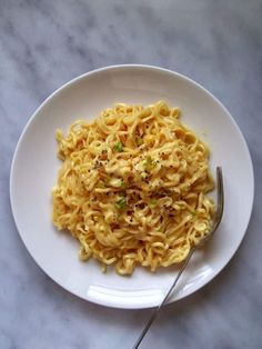 a white plate topped with pasta and a fork on top of a marble countertop