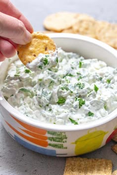 a hand dipping a cracker into a bowl of dip