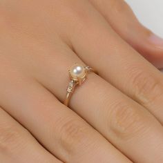 a woman's hand with a pearl and diamond ring on top of her finger