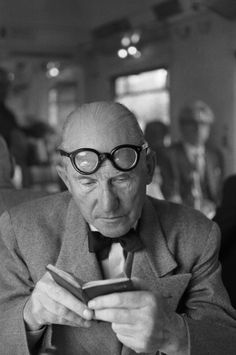 an old man wearing glasses looking at his cell phone while sitting in front of him