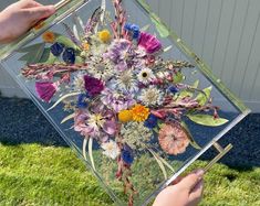 a person holding a vase with flowers in it on the grass next to a fence