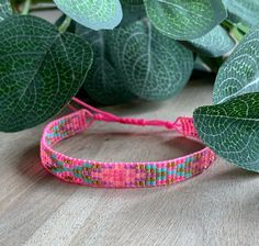 a close up of a bracelet on a table with leaves in the background and a plant behind it