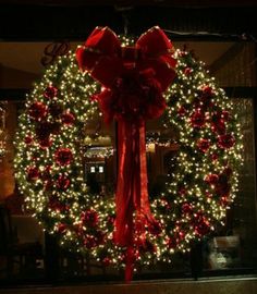 a christmas wreath with red bows and lights in the background, is lit up at night