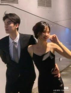 two people standing next to each other in front of some stairs and one person wearing a suit