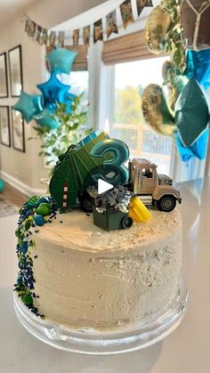 a birthday cake with cars on it and streamers hanging from the ceiling in the background