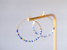 "Creole brass earrings gilded with fine gold, embellished with fine Japanese Miyuki glass beads in shades of blue and gold. Creole diameter: 2.7 cm The gilding is made by a Parisian gilder craftsman on a raw brass base. All materials used comply with European standards. Jewel delivered in gift pouch. Neat sending by followed mail https://www.instagram.com/ateliervivienne https://atelier-vivienne.com TO SEE THE ENTIRE \"CREOLES\" COLLECTION: https://www.etsy.com/fr/shop/AtelierVivienne?ref=seller Brass Jewelry With Tiny Beads In Dangle Shape, Blue Beaded 14k Gold-filled Jewelry, Blue Beaded Brass Earrings As Gift, Handmade Blue Hoop Jewelry, Gift Blue Beaded Brass Earrings, Handmade 14k Gold Filled Round Beaded Earrings, Blue Beaded Brass Earrings, Gold Plated Earrings With Gold Beads As A Gift, Bohemian Blue 14k Gold-filled Jewelry