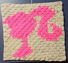 a crocheted square with pink and beige squares on it hanging from a hook