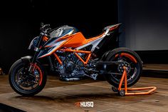 an orange and black motorcycle parked on top of a wooden floor